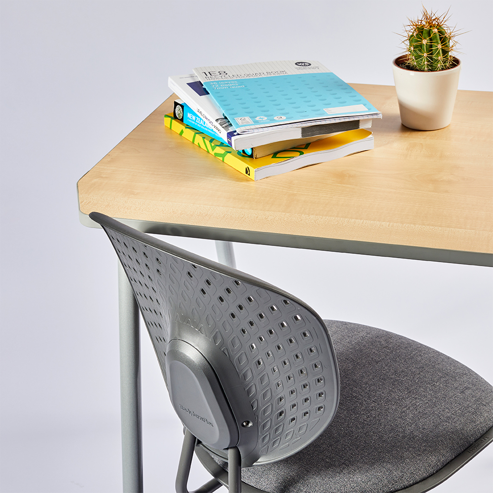 Bodyfurn Flex padded gaslift chair beside student desk with books on top.