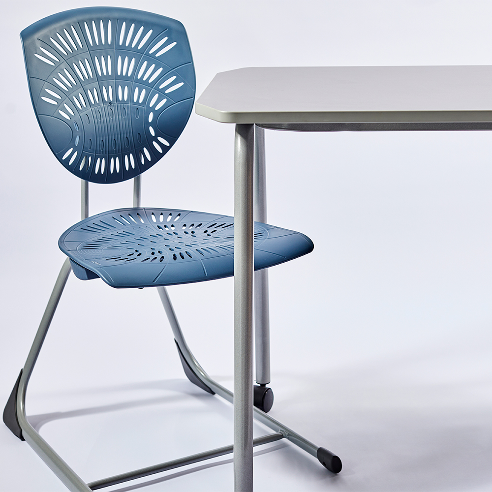Blue Bodyfurn sled chair positioned beside a classroom table in a studio setting.