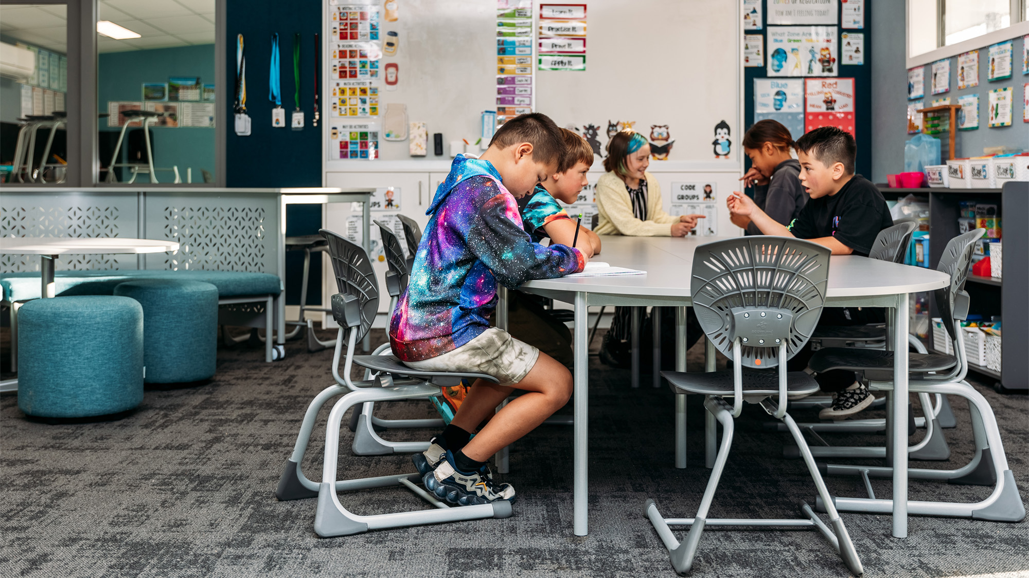 Primary school students working collaboratively in a modern classroom with Furnware Bodyfurn.Flex chairs and learning tables