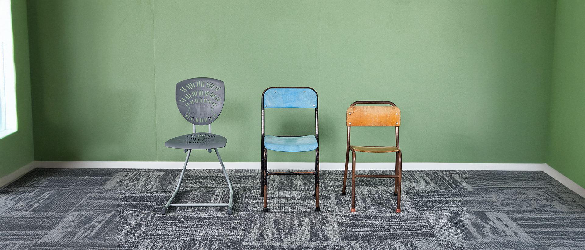 Three school chairs from different eras displayed against a green classroom wall, showing Furnware’s design evolution over time.