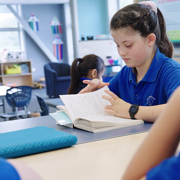 Student reading a book at a classroom table at Elmwood Normal School.