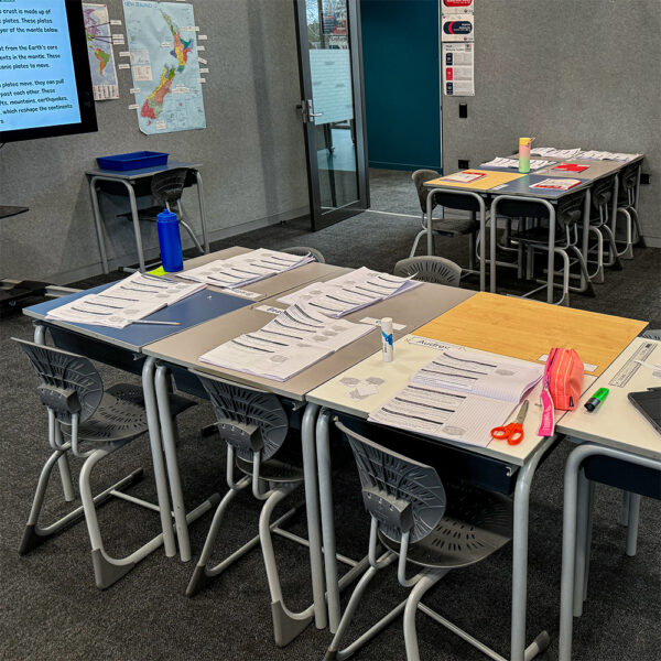 Individual desks arranged in groups with grey Bodyfurn chairs and student workbooks at Cobham Intermediate.