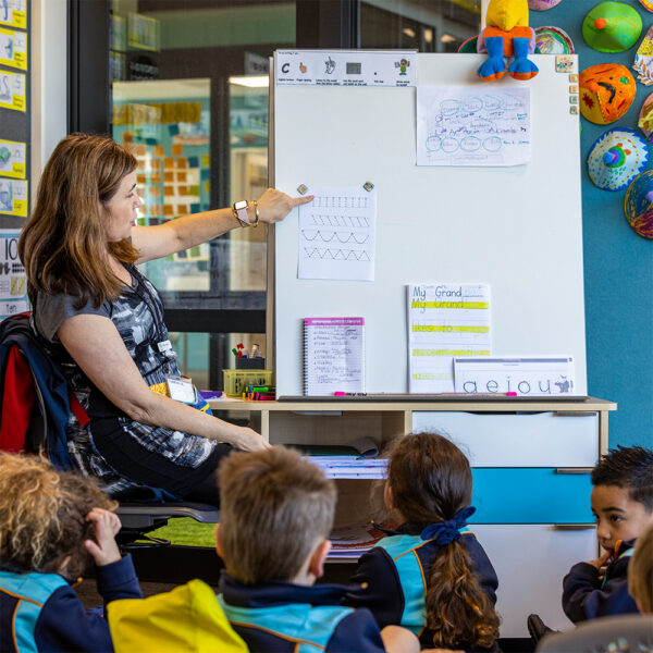 Teacher pointing to handwriting patterns on a whiteboard while students gather for mat time at Putaruru Primary.